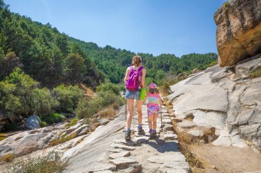 from behind daughter and mother hiking on a stones trail in Camo