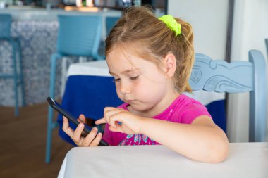 little girl touching mobile phone sitting in restaurant