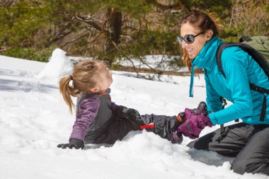 mother placing boot to girl smiling together on the snow