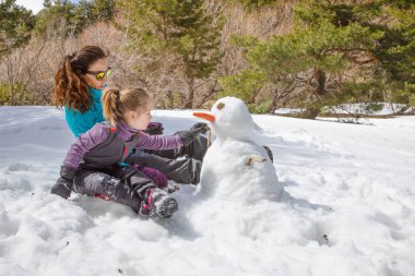 woman and little girl making a snowman sitting in nature