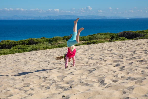 Bambina che fa la verticale sulla duna con l'Africa all'orizzonte — Foto Stock