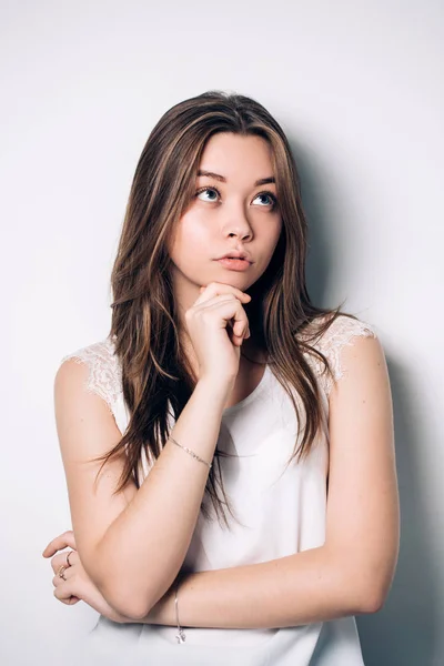 Retrato de la hermosa joven sobre un fondo blanco. Piensa mirando hacia arriba — Foto de Stock