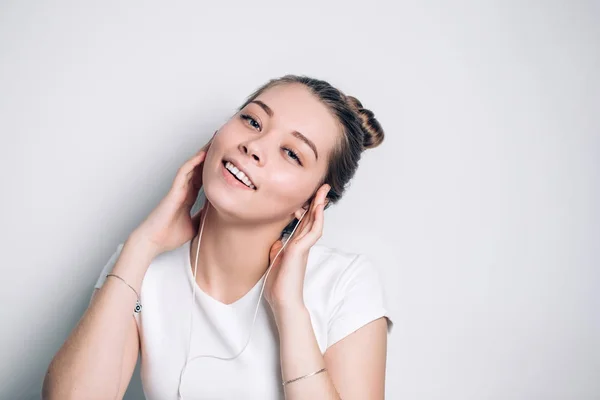 Bella giovane donna in cuffia che ascolta musica e canta su sfondo bianco — Foto Stock