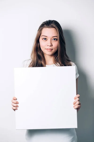 Joven mujer sonriente sosteniendo una hoja de papel en blanco para publicidad — Foto de Stock