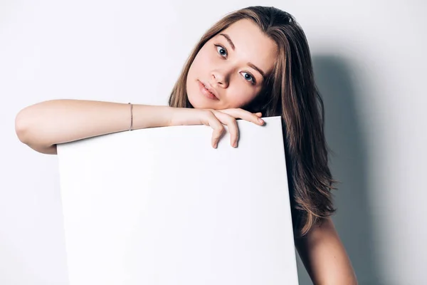 Joven mujer sonriente sosteniendo una hoja de papel en blanco para publicidad, primer plano — Foto de Stock