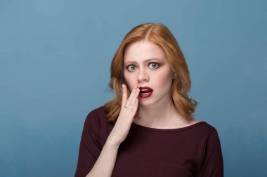 Güzel sürpriz ve şok kıvırcık saçlı kız. Mavi bir arka plan üzerinde parlak makyaj ile genç bir kadın. Etkileyici yüz hatları, duygular, karışıklık.