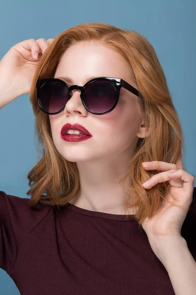 Bela ruiva menina em óculos de sol pretos em um fundo azul close up retrato — Fotografia de Stock