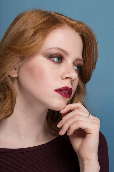 Pensive redhead girl looking to side, close-up portrait on blue background. — Stock Photo, Image