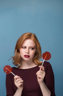 Mavi bir arka plan üzerinde iki kırmızı lolipop genç bir kadın portresi. Seçim kavramı, copys hızı.