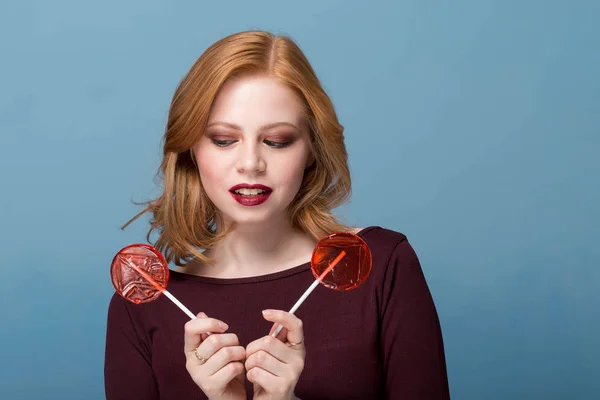 时尚肖像女人吹嘴唇两个红色的棒糖在彩色背景 — 图库照片
