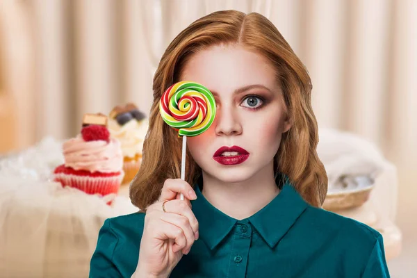 红头发美丽的女孩在绿色衬衫与多色圆糖果院长关闭他的眼睛对蛋糕的背景从莓果 — 图库照片