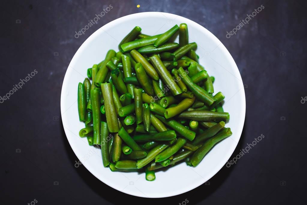 Cooked green beans in white plate on black background, Close up, top view. healthy food, proper nutrition.