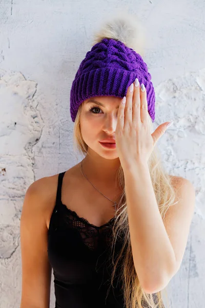 A beautiful woman closes one eye with a hand. The girl in the purple hat