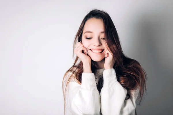 Sonriente mujer feliz muerde el labio con una sonrisa y mira hacia abajo en el fondo blanco. Emociones —  Fotos de Stock