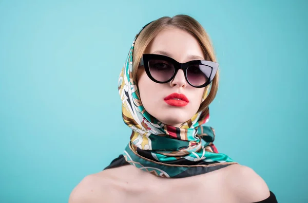 Primer plano de mujer joven con estilo en gafas de sol y chal de colores, pañuelo para la cabeza, bufanda contra fondo azul. Hermosa modelo femenina — Foto de Stock