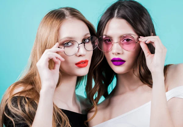 Dos hermosas modelos de mujeres en gafas, con maquillaje y cara de piel limpia y saludable en azul —  Fotos de Stock