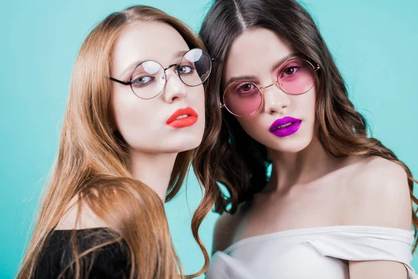 Stüdyo kız portresi. İki güzel kadın parlak makyaj ve mavi arka plan, yuvarlak gözlük ile kapatın. Yatay.
