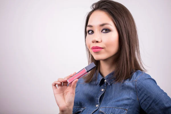 Wanita cantik dengan riasan lembut memegang tangannya pada lipstik merah muda dan lip gloss. Narablog kecantikan, penata rias — Stok Foto