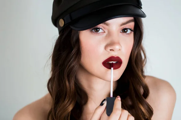 Verleidelijke mooie jonge brunette vrouw met behulp van lip borstel voor het toepassen van rode lippenstift op haar lippen. Reclame lippenstift, lipgloss, cosmetica. — Stockfoto