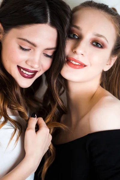 Twee mooie brunette en blonde vrouwen, vriendinnen met professionele make-up kijken camera met glimlach op witte achtergrond. — Stockfoto