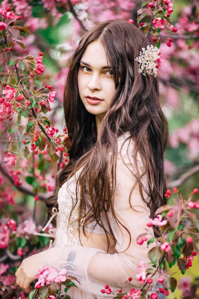 Portrait de belle femme brune dans une robe de mariée en dentelle de boudoir beige, décoration pour cheveux longs, à côté de l'arbre Sakura aux fleurs roses — Photo