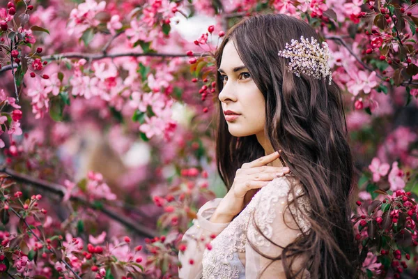 Belle jeune mariée mignonne en dentelle de boudoir robe transparente, avec décoration sur les cheveux, près de l'arbre fleurit avec des fleurs roses, profil, horizontal — Photo