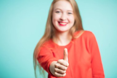 Üzerinde mavi bir arka plan, odak parmak başparmak mutlu genç kadın ortaya