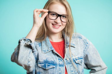 kadın gözlük mavi bir arka plan üzerinde kameraya bir gülümseme ile görünüyor.