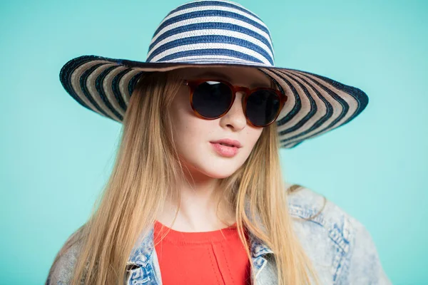 Young blonde woman with sunglasses and striped hat on blue background — Stock Photo, Image