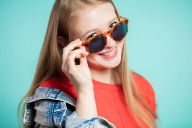 Neşeli kız yakından bir gülümseme ile kameraya onun güneş gözlüğü düşürürken görünüyor