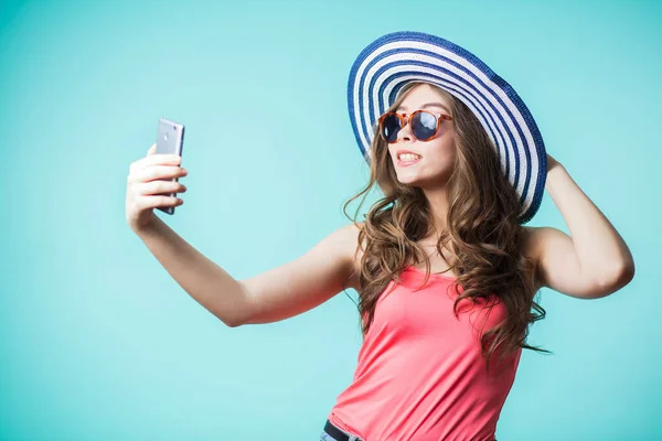 Schattige brunette meisje neemt een selfie. Ze glimlacht wijd. Gelukkige vrouw draagt een gestreepte hoed en roze top — Stockfoto