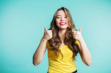 Jest Yaşasın hevesli motive genç bir kadın. Sarı tişört ve kırmızı dudaklar geniş mavi arka plan üzerinde gülümseyen güzel esmer kız