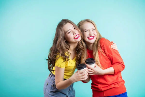 Alegre dos chicas con tazas de papel de café con una sonrisa mirando a la cámara, riendo, regocijándose —  Fotos de Stock