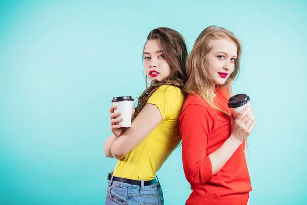 Две женщины, улыбающиеся спиной к спине с бумажными чашками кофе — стоковое фото