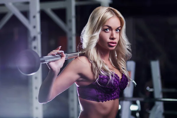 Very beautiful sexy girl, model, blonde with tanned skin in a purple underwear in gym squatting with kettlebells, dumbbells, close-up, looking at camera, fitness, cross fit, sport, — Stock Photo, Image