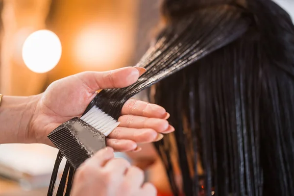 Close up de cabeleireiro mulher aplicando cuidados com o cabelo com um pente seu cliente . — Fotografia de Stock