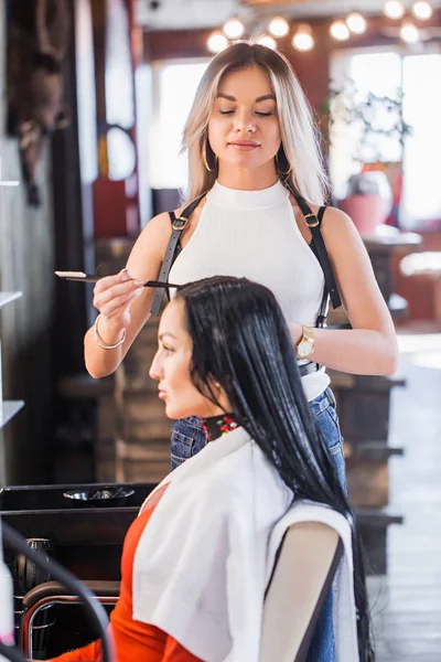 Hermosa peluquera rubia hace el Spa en el pelo largo morena mujer — Foto de Stock