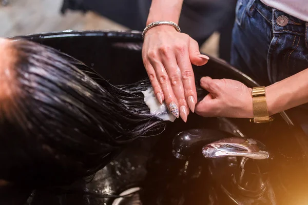 Il primo piano di parrucchiere di mani applica una maschera bianca ai clienti i capelli scuri lunghi. Cura — Foto Stock
