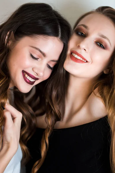 Zwei schöne brünette und blonde Frauen, Freundinnen mit professionellem Make-up blicken mit einem Lächeln auf weißem Hintergrund in die Kamera. Freude, Lachen, Glück, Freundschaft — Stockfoto