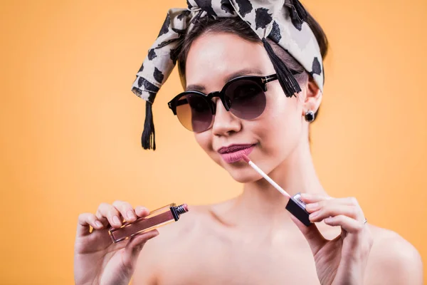 Menina bonita em óculos de sol segurando batom na mão, brilho labial e olhando com um sorriso para a câmera — Fotografia de Stock