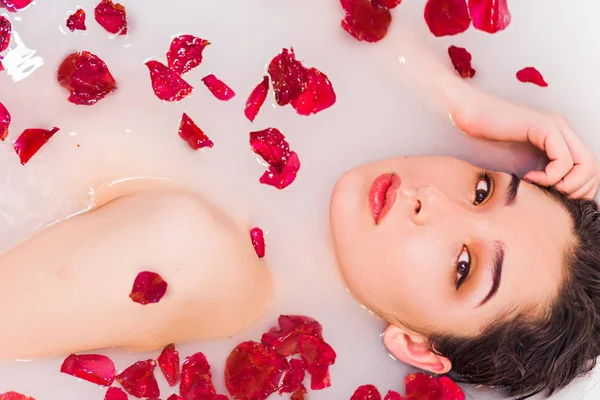 Güzel seksi genç kadın çiçek yaprakları ile banyoda ve kameraya bakarak yakın çekim — Stok fotoğraf
