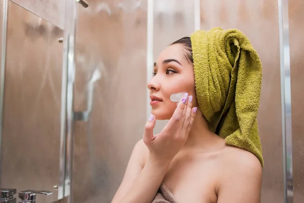 Wanita muda cantik menerapkan perawatan krim kosmetik di wajahnya — Stok Foto