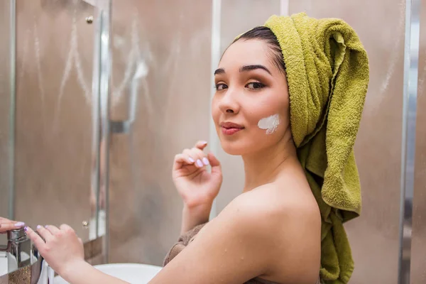 Potret seorang wanita berambut cokelat muda menerapkan krim atau masker wajah di kamar mandi — Stok Foto