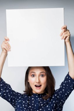 bir kız, yükseltir net kare kağıt etiket elleriyle, ağzını aç ve beyaz bir arka planda, duygular, gözleri ile üst portresi gülümse,