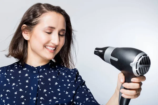 Seorang wanita muda yang cantik merasa bahagia saat menggunakan pengering rambut dan sikat rambut — Stok Foto