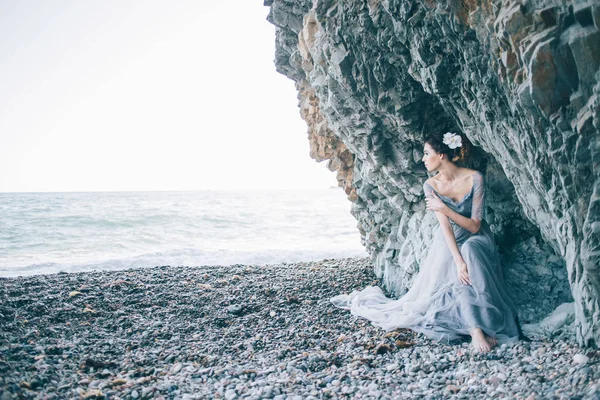 Bella ragazza bruna in abito blu, fiore bianco in capelli seduto vicino alla scogliera, il mare, il profilo di visualizzazione , — Foto Stock