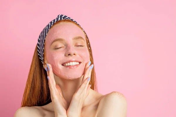 Wanita cantik dengan masker wajah di latar belakang merah muda — Stok Foto