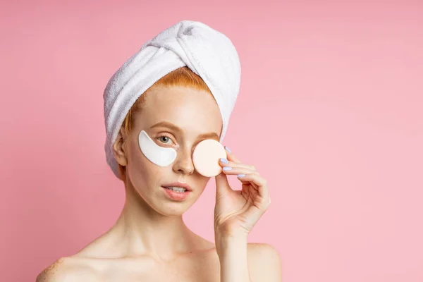 Tiro de mujer joven aplica parches para los ojos y la celebración de esponja cosmética — Foto de Stock