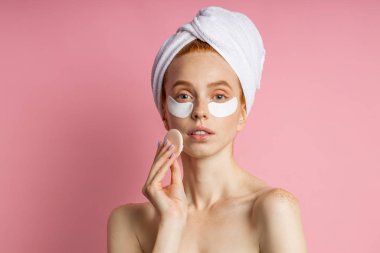 Göz altı bantlı genç bir kadın pembe arka planda izole edilmiş.