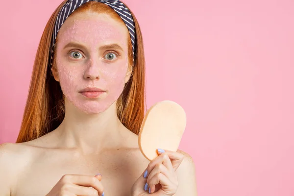 Hermosa mujer con máscara facial sobre fondo rosa — Foto de Stock